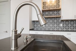 Close-up view of a modern stainless steel kitchen faucet with sleek design against tiled backsplash.